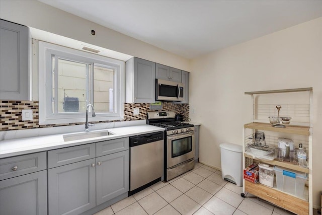 kitchen with stainless steel appliances, light tile patterned flooring, sink, backsplash, and gray cabinets