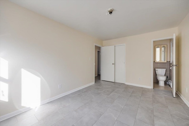 unfurnished bedroom featuring light tile patterned flooring, ensuite bath, and a closet