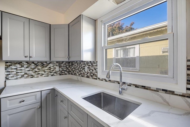 kitchen featuring gray cabinets, sink, light stone counters, and tasteful backsplash