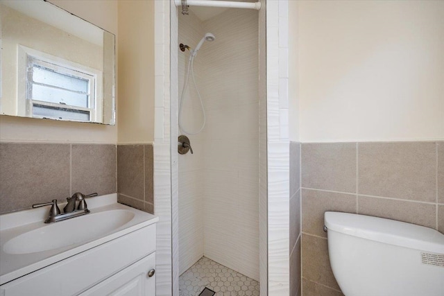 bathroom with tile walls, tiled shower, vanity, and toilet