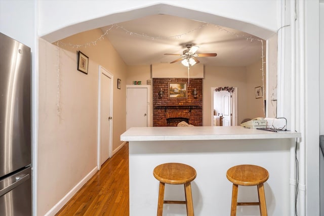 kitchen with a peninsula, a kitchen breakfast bar, a ceiling fan, and freestanding refrigerator