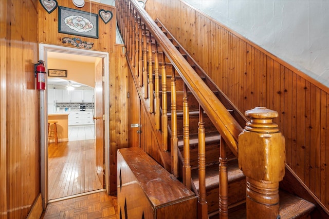 stairs featuring ceiling fan and wood walls