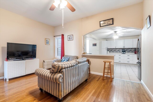 living room featuring light wood-style flooring, radiator heating unit, arched walkways, and ceiling fan