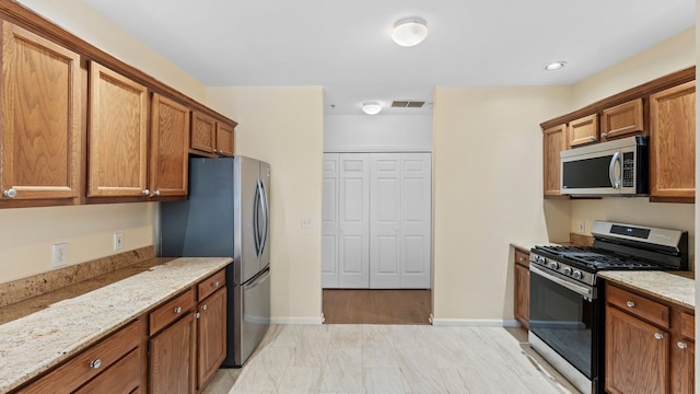 344 The Promenade Unit 344, Edgewater, NJ 07020 - kitchen with baseboards, appliances with stainless steel finishes, brown cabinets, and light stone countertops