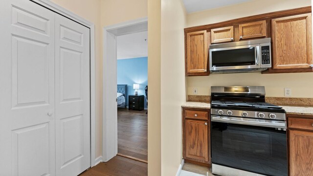 344 The Promenade Unit 344, Edgewater, NJ 07020 - kitchen featuring appliances with stainless steel finishes, light stone counters, brown cabinets, and wood finished floors