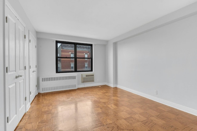 spare room featuring light parquet flooring, an AC wall unit, and radiator heating unit