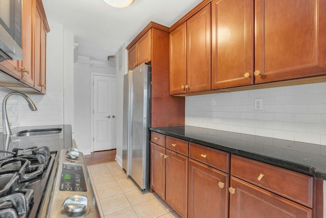 kitchen with appliances with stainless steel finishes, dark stone counters, light tile patterned flooring, and backsplash