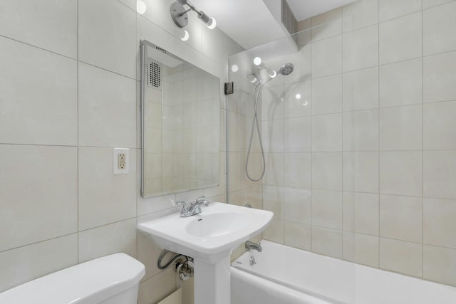 full bathroom with tile walls, sink, tiled shower / bath combo, and toilet