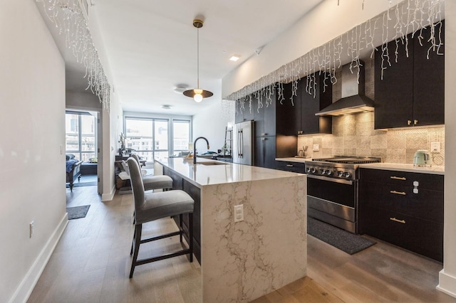 kitchen featuring a sink, light wood-style floors, appliances with stainless steel finishes, wall chimney range hood, and tasteful backsplash
