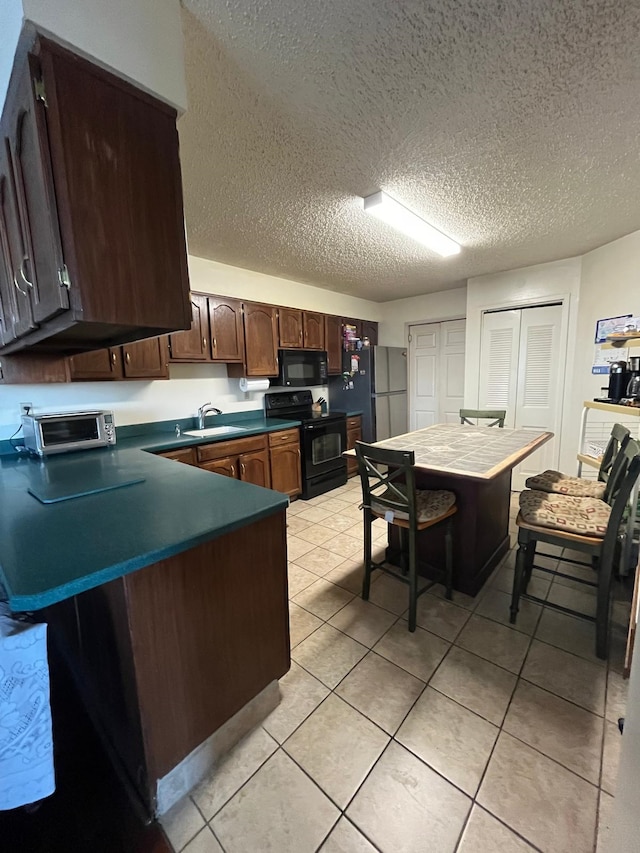 kitchen with dark countertops, light tile patterned floors, a peninsula, black appliances, and a sink