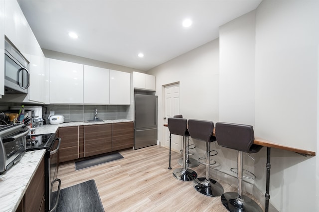 kitchen with white cabinetry, appliances with stainless steel finishes, backsplash, light wood-type flooring, and sink