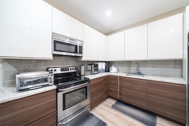 kitchen with white cabinetry, appliances with stainless steel finishes, backsplash, and light wood-type flooring