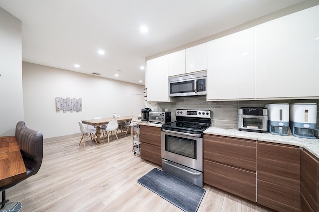 kitchen featuring tasteful backsplash, light stone counters, stainless steel appliances, light hardwood / wood-style floors, and white cabinets