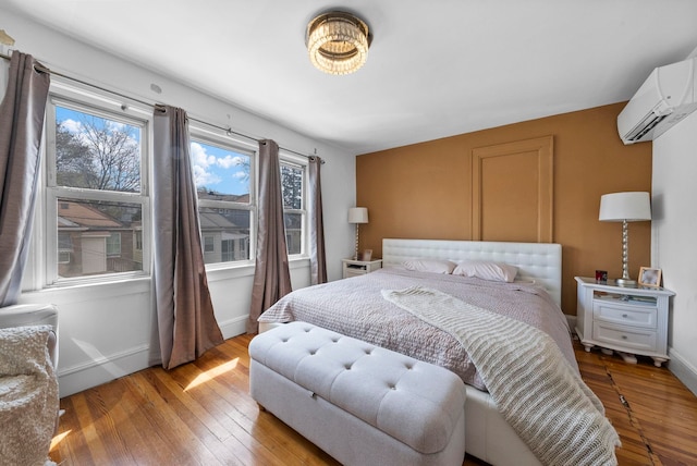bedroom with light wood-style flooring, an AC wall unit, and baseboards