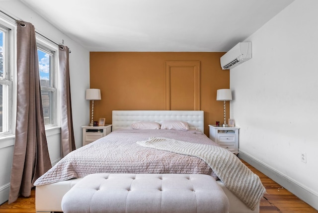 bedroom with baseboards, light wood-type flooring, and a wall mounted air conditioner