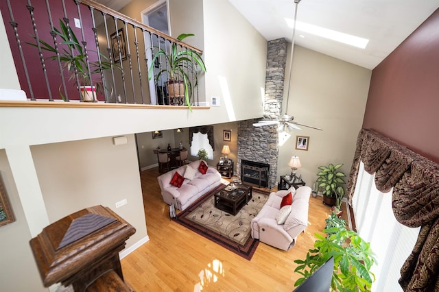 living room featuring high vaulted ceiling, a skylight, ceiling fan, a fireplace, and wood-type flooring