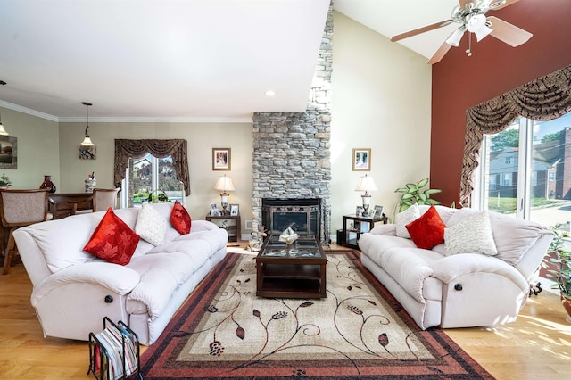 living room featuring a stone fireplace, crown molding, vaulted ceiling, light hardwood / wood-style flooring, and ceiling fan