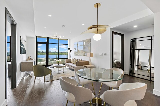 dining area featuring dark wood-type flooring, a water view, a wall of windows, and a chandelier