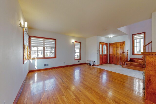 unfurnished living room with plenty of natural light, wood finished floors, stairs, and baseboards
