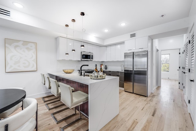 kitchen featuring kitchen peninsula, pendant lighting, stainless steel appliances, and white cabinets