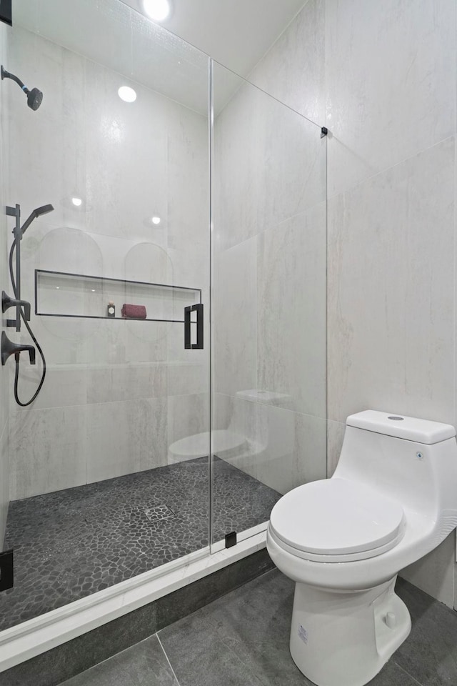 bathroom with tile walls, toilet, walk in shower, and tile patterned flooring