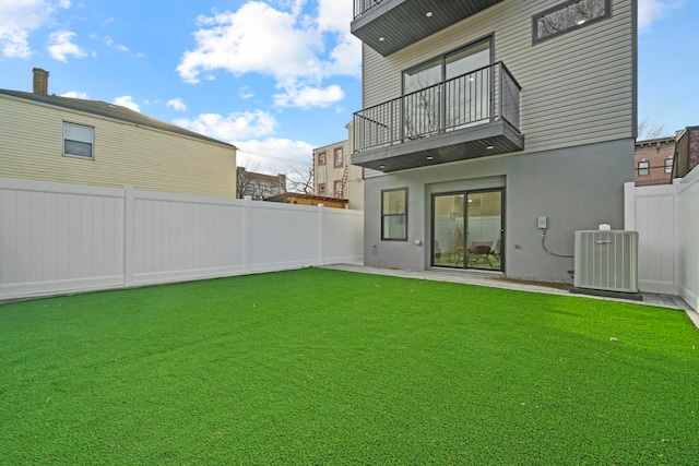 rear view of property with a balcony, central air condition unit, and a yard