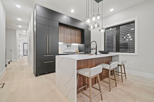 kitchen featuring light hardwood / wood-style flooring, decorative light fixtures, backsplash, a kitchen island with sink, and a breakfast bar