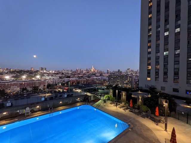 community pool with a view of city lights, fence, and a patio