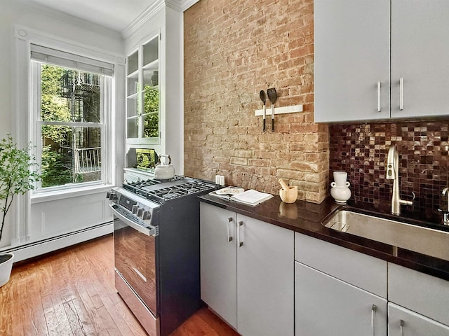 112 Wayne St Unit 2-A, Jersey City, NJ 07302 - kitchen with stainless steel range with gas stovetop, a baseboard radiator, dark countertops, wood finished floors, and crown molding
