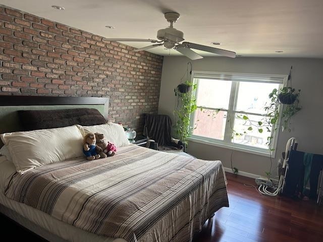 bedroom featuring ceiling fan, dark wood-type flooring, and brick wall