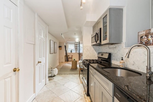 kitchen with stainless steel appliances, a sink, gray cabinets, backsplash, and dark stone counters