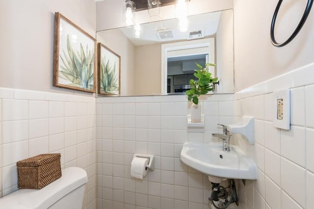 bathroom with tile walls, toilet, and a wainscoted wall