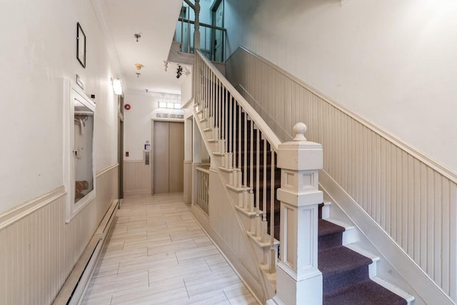 stairs with a wainscoted wall, elevator, and a baseboard heating unit