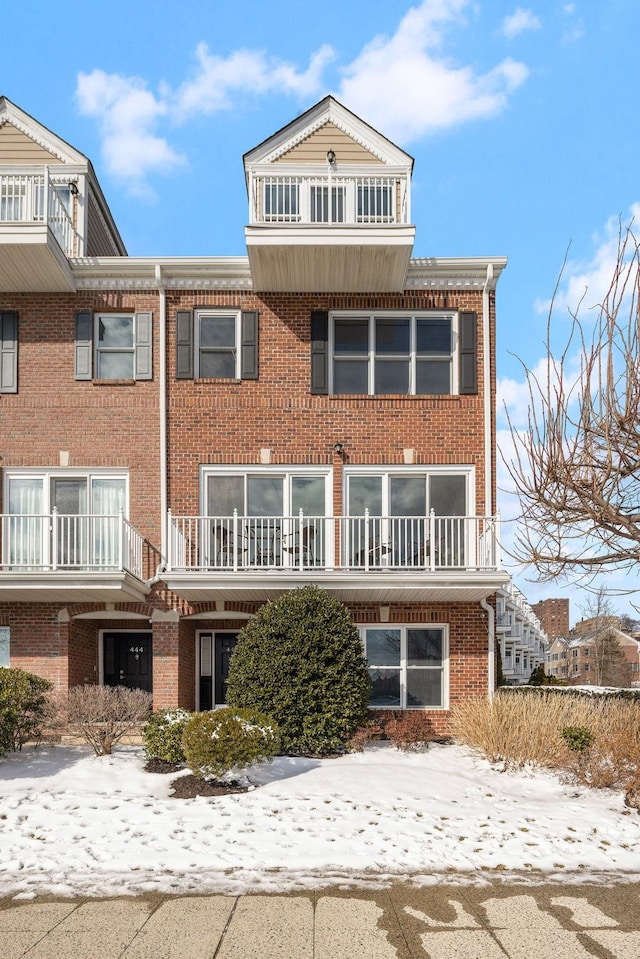 snow covered property featuring brick siding and a balcony
