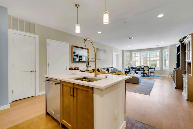 kitchen with visible vents, stainless steel dishwasher, a kitchen island with sink, open floor plan, and light countertops