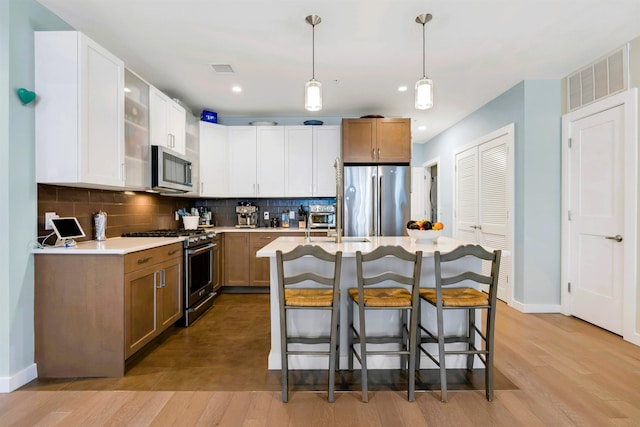 kitchen featuring a breakfast bar area, visible vents, appliances with stainless steel finishes, baseboards, and light wood finished floors