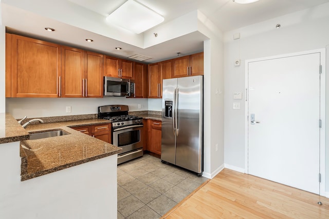 kitchen with stainless steel appliances, dark stone counters, sink, kitchen peninsula, and light hardwood / wood-style flooring