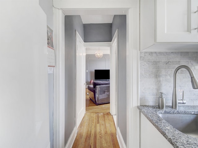 hall with light wood-style floors, a notable chandelier, and a sink