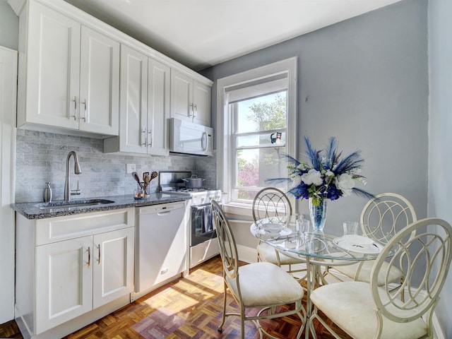 kitchen featuring dark stone countertops, tasteful backsplash, white appliances, white cabinets, and a sink