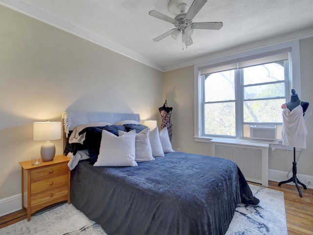 bedroom featuring baseboards, radiator, light wood-style floors, and a textured ceiling