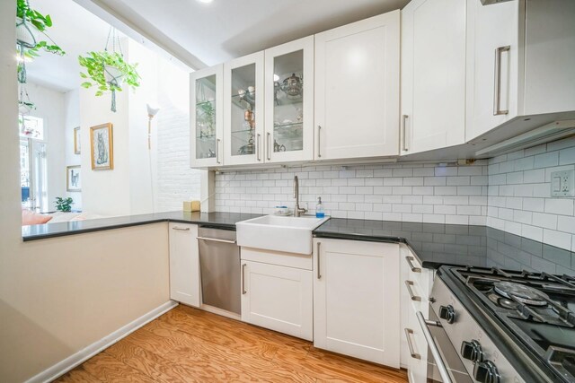 kitchen with appliances with stainless steel finishes, decorative backsplash, a sink, and light wood-style floors