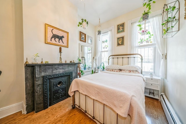 bedroom with light wood-type flooring, baseboards, a tiled fireplace, and baseboard heating
