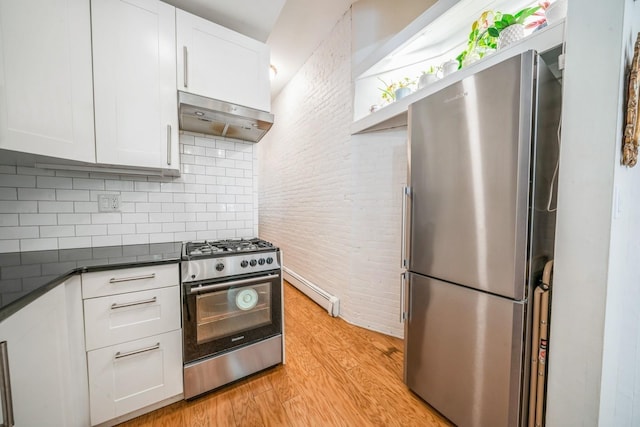 kitchen with dark countertops, light wood-type flooring, white cabinetry, under cabinet range hood, and appliances with stainless steel finishes