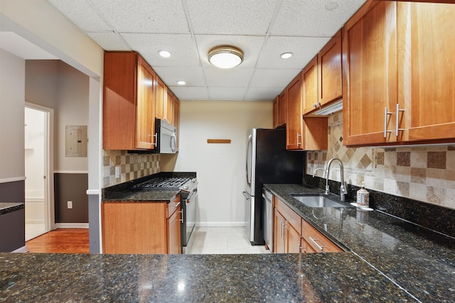 kitchen with appliances with stainless steel finishes, brown cabinets, a sink, baseboards, and dark stone countertops