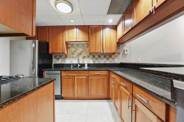 kitchen with appliances with stainless steel finishes, light tile patterned floors, a sink, dark stone counters, and a drop ceiling