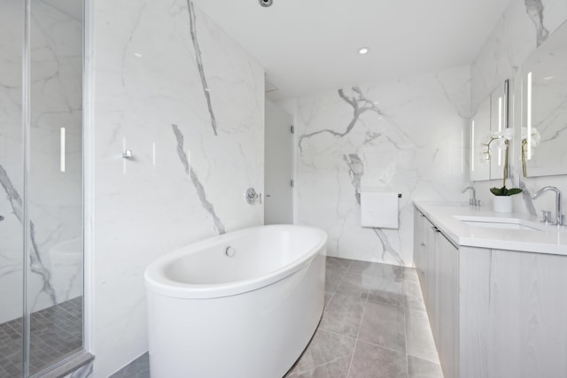 bathroom featuring double vanity, stone wall, a freestanding tub, and a sink