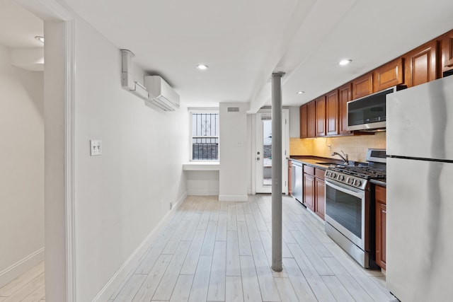 kitchen with stainless steel appliances, tasteful backsplash, sink, a wall unit AC, and light hardwood / wood-style flooring