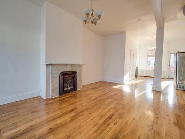 unfurnished living room featuring a chandelier, a tile fireplace, baseboards, and wood finished floors