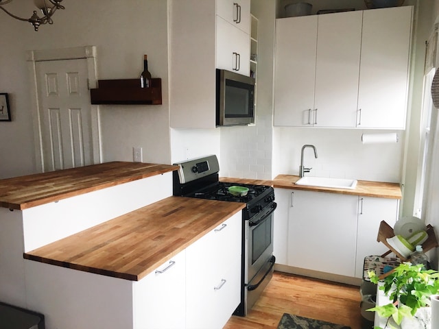 kitchen with a sink, decorative backsplash, white cabinets, appliances with stainless steel finishes, and wood counters