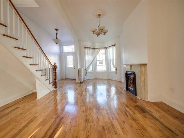 foyer entrance featuring radiator, wood finished floors, baseboards, an inviting chandelier, and stairs